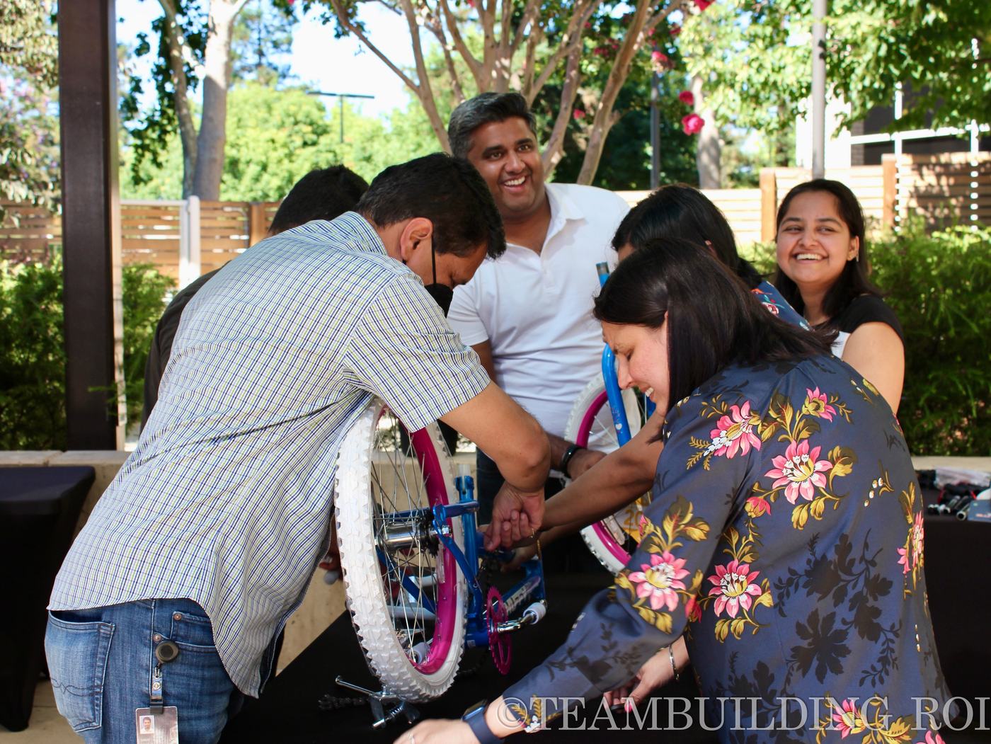 A team smiles while working on a bike together outdoors.