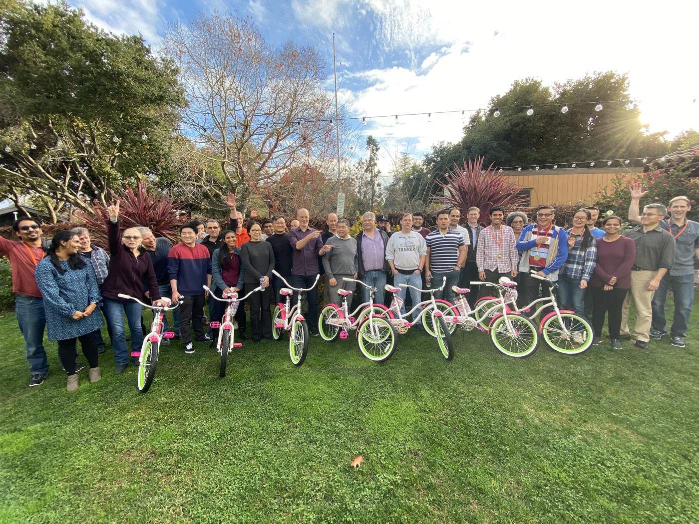 A large team celebrates behind a row of bicycles they built together